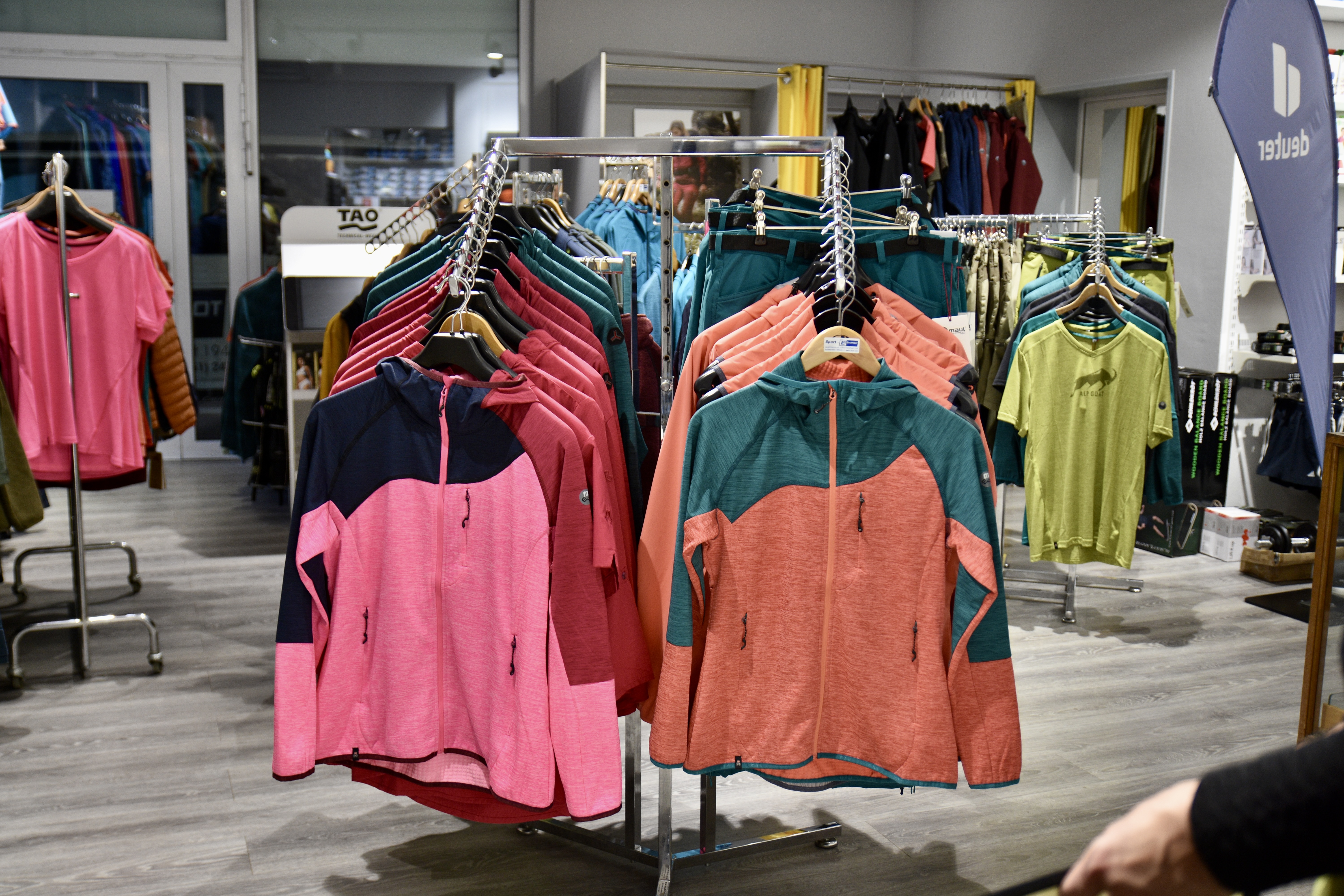 Farbige Outdoorjacken und Shirts auf Kleiderständern im Sport-Gebhardt-Laden